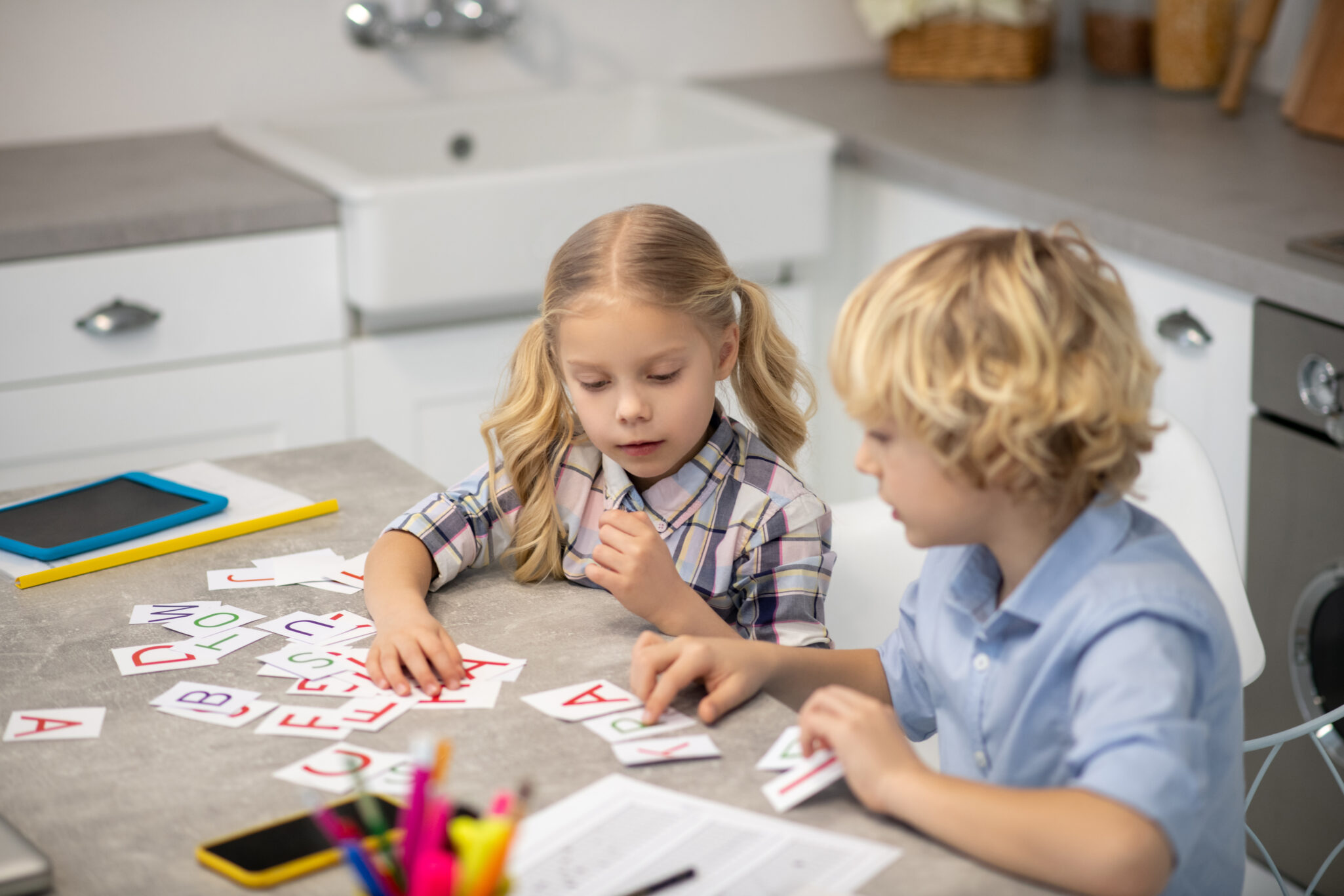 Two blond kids learning letters and looking interested